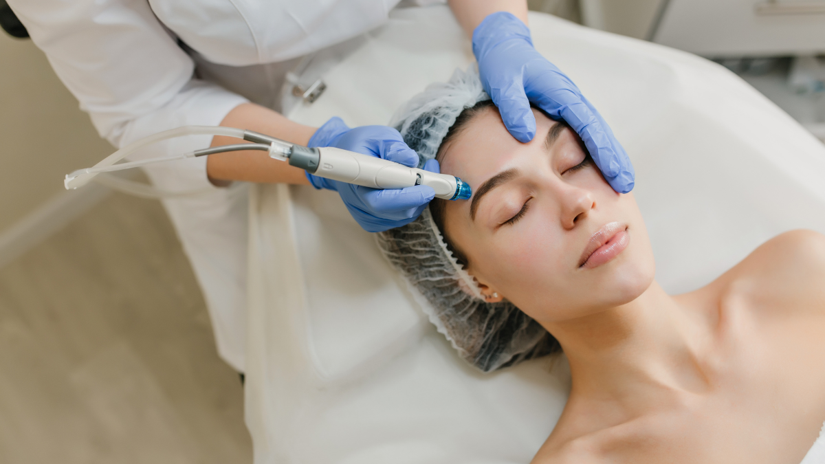 Procedimento estético em clínica: profissional com luvas azuis realiza tratamento no rosto de uma cliente com aparelho e máscara de proteção, em ambiente limpo e iluminado.