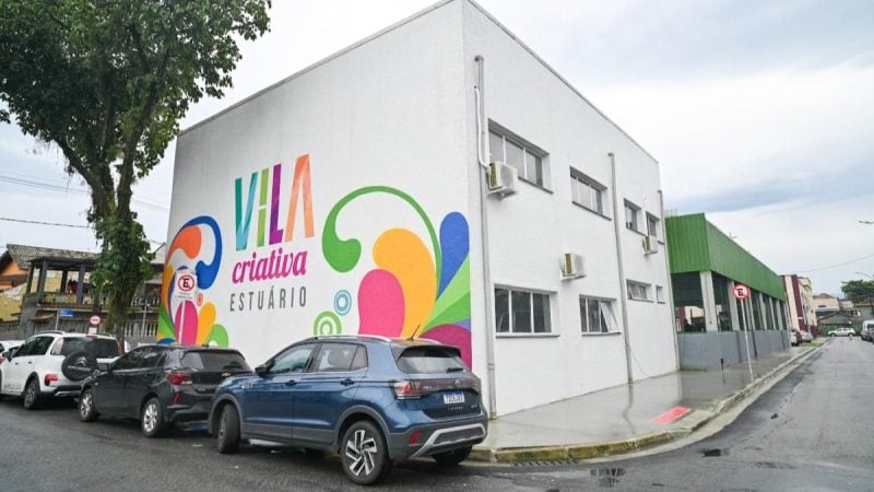 Fachada do prédio da Vila Criativa no Estuário, com pintura colorida e a expressão “Vila criativa Estuário” no muro, carros estacionados e rua ao redor.