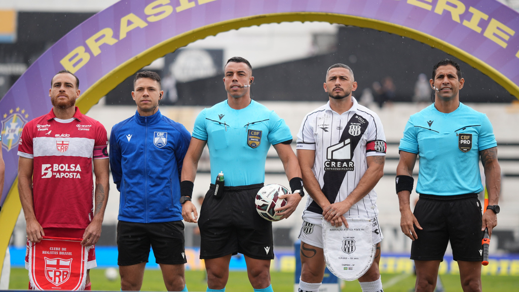 Ponte volta a vencer: Jogadores de Ponte Preta e CRB em foto de arbitragem, com bola de futebol no centro e faixa roxa “BRASILEIRÃO SÉRIE B”, registrando o confronto da partida Ponte Preta x CRB no estádio.