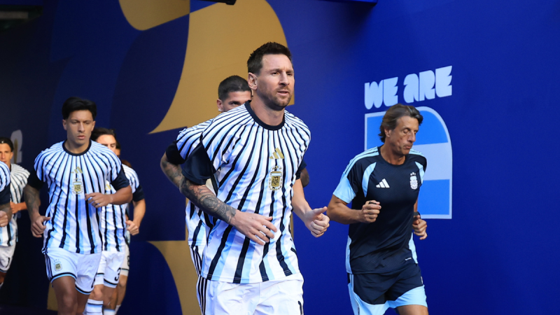 Messi desfila com camisa especial listrada durante jogo de despedida da Argentina, em um evento esportivo com jogadores ao fundo e cenário azul
