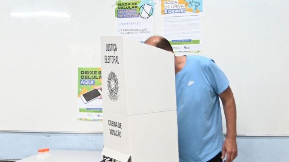 Pessoa depositando voto em urna eleitoral em contexto de explicação sobre o Sigilo do voto nas eleições 2026, com materiais informativos ao fundo (foto: Reprodução / TRE-SP).