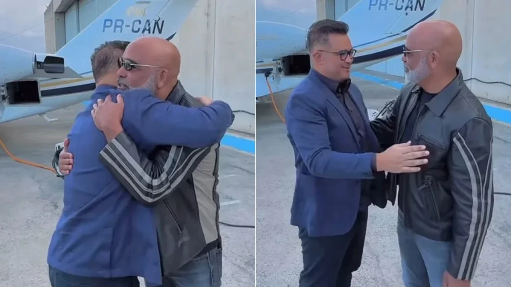 Rick e Bruno Avelar se cumprimentam antes de entrarem em um helicóptero em Santa Catarina. Foto mostra os dois ao lado da aeronave.