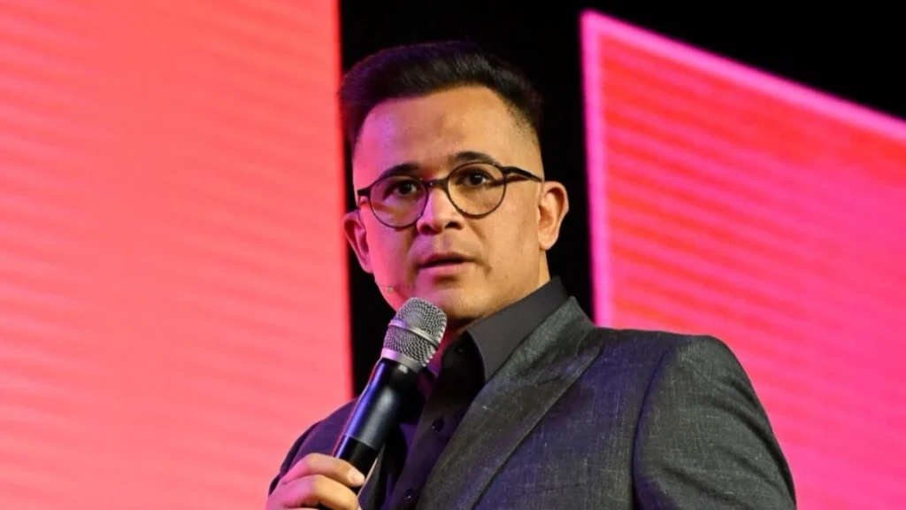 Bruno Avelar em palestra, segurando um microfone e falando em um palco com iluminação rosa, no contexto de desaparecimento.