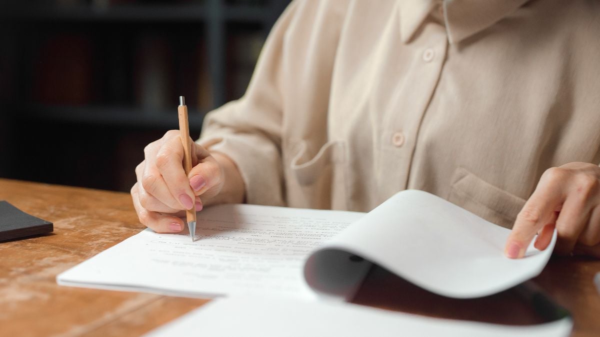 Guia do Enem: estudante escrevendo em uma folha de exercícios sobre uma mesa, com caderno aberto, representando dicas, simulados e ferramentas para os estudos.
