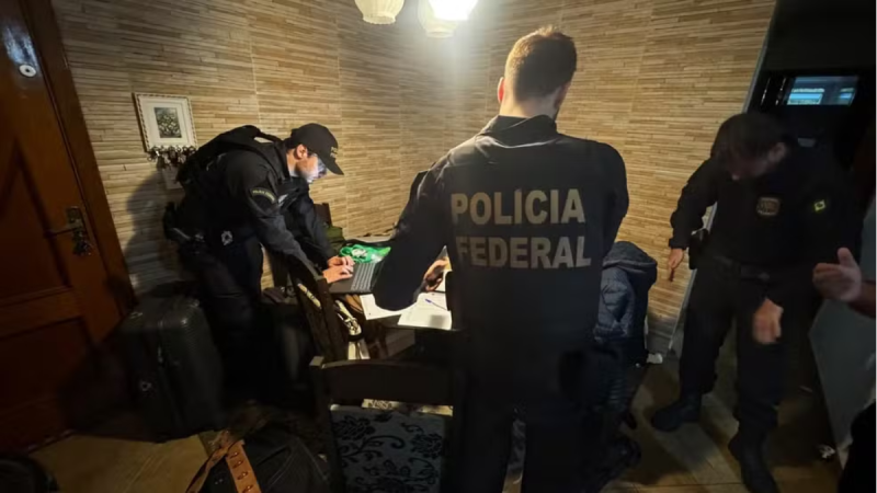 Operação Rota Diplomática: Operação da PF mira esquema de contrabando de eletrônicos via Viracopos: agentes da Polícia Federal realizam abordagem em ambiente interno, com documentos e equipamentos sobre a mesa.