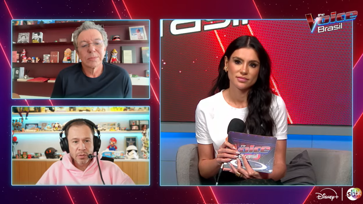 Captura de ecrã de uma transmissão do programa The Voice Brasil dividida em três ecrãs: no lado esquerdo, em videochamada, surgem o diretor Boninho (em cima) e o apresentador Tiago Leifert (em baixo); no ecrã maior, à direita, a apresentadora e jornalista Gaby Cabrini surge num estúdio a segurar cartões e o microfone do programa.