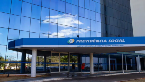 Fachada do edifício-sede do Instituto Nacional do Seguro Social (INSS) e da Previdência Social, com paredes espelhadas de vidro azul, cobertura na entrada principal e colunas de sustentação sob um céu limpo.