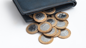 Carteira de couro azul aberta com moedas ao lado, incluindo moedas brasileiras, em fundo claro, destacando dinheiro e numismática.
