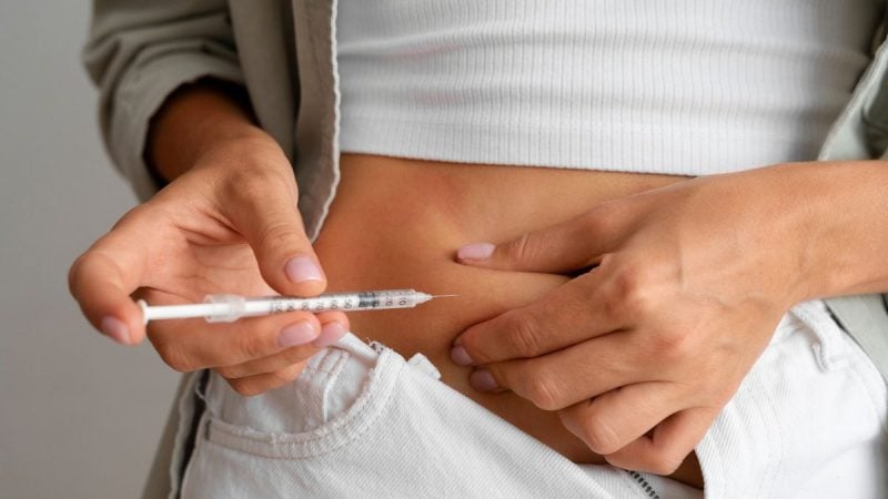 Mãos de uma pessoa segurando uma seringa com agulha próxima ao abdômen, em alerta sobre por que a tirzepatida em pó não é recomendada pela Anvisa e os riscos do uso inadequado.