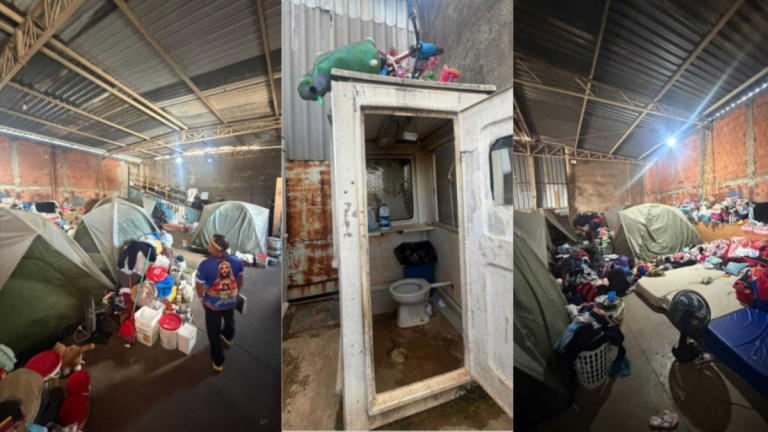 Interior de um abrigo com tendas e pessoas em situação de acolhimento, ao lado de uma instalação sanitária com vaso e pia em ambiente de galpão