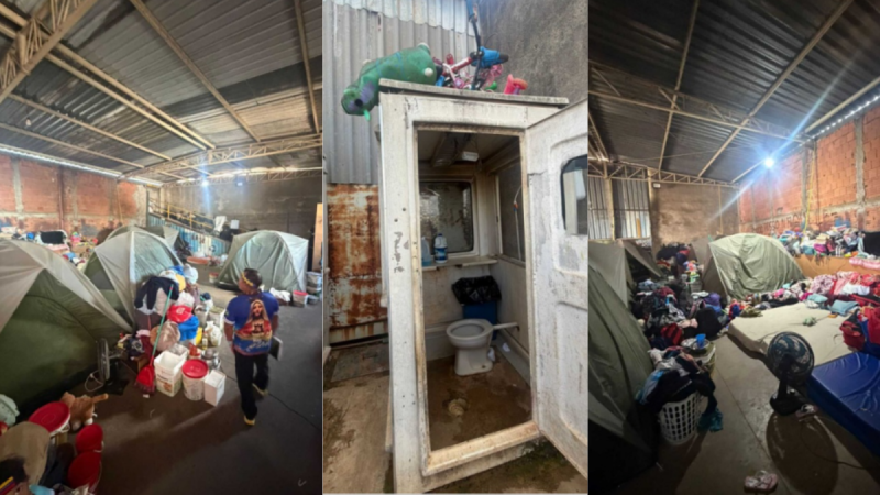 Interior de um abrigo com tendas e pessoas em situação de acolhimento, ao lado de uma instalação sanitária com vaso e pia em ambiente de galpão