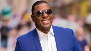 Netinho de Paula sorrindo com óculos escuro, o cantor veste um paletó azul e camiseta branca
