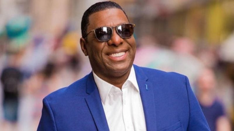 Netinho de Paula sorrindo com óculos escuro, o cantor veste um paletó azul e camiseta branca