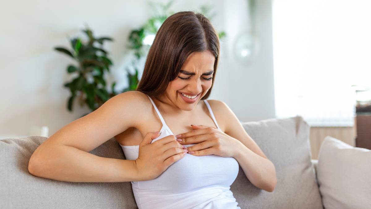Mulher leva a mão ao peito e demonstra preocupação com possíveis sintomas cardiovasculares