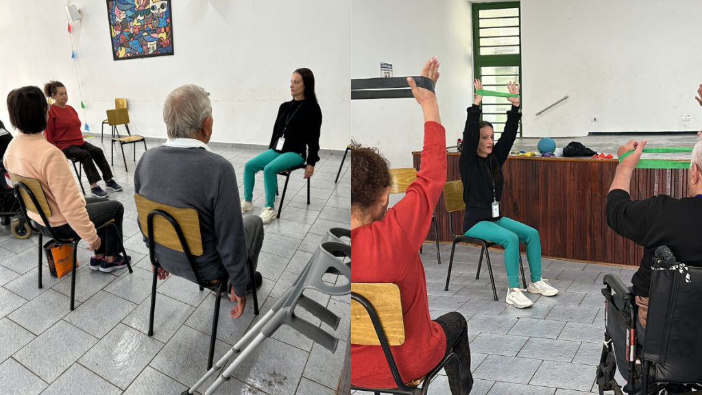 Participantes sentados em cadeiras durante uma atividade em grupo, com uma instrutora ao fundo e exercícios de alongamento e gestos com os braços em uma sala com piso de cerâmica e lousa.