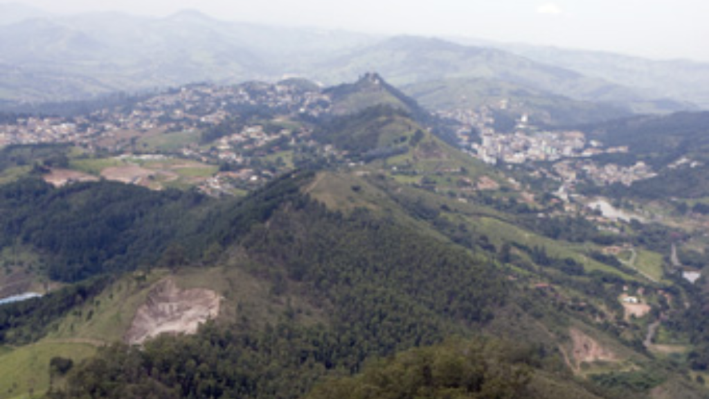 Vista panorâmica de uma paisagem montanhosa com vales e pequenas comunidades ao fundo, em uma região verde com colinas cobertas por vegetação e serras ao longo do horizonte.