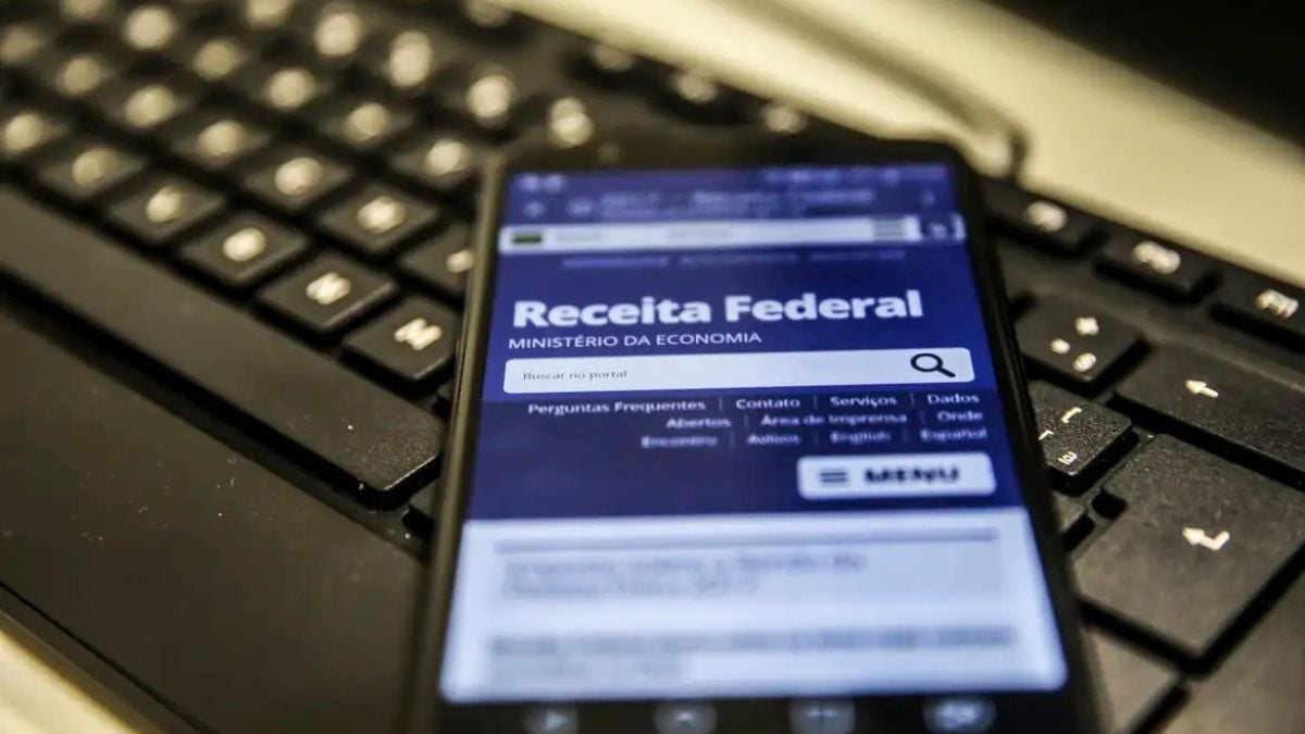 Notícia sobre malha fina: tela do celular com o sistema da Receita Federal (Ministério da Economia) ao lado de um teclado, em imagem de reportagem.