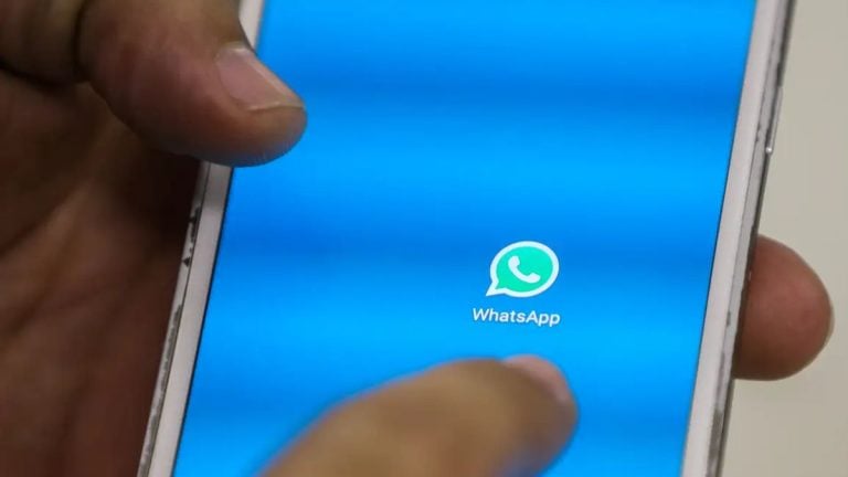 Smartphone com o aplicativo WhatsApp aberto na tela azul, com o ícone do WhatsApp central e mãos segurando o celular durante o uso