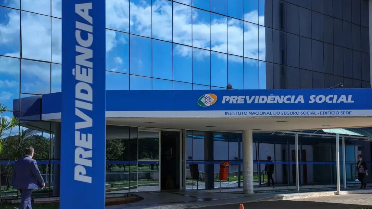 Fachada do INSS com placa “PREVIDÊNCIA SOCIAL” em Brasília, ao lado da coluna “PRÊVIDÊNCIA SOCIAL”, com trabalhadores ao fundo; INSS pagará benefício a trabalhadoras afastadas por violência doméstica.