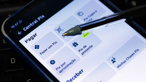 Celular com tela do app Pix aberto, mostrando opções como Pagar, Fazer um Pix, Pix de presente e Aproximação, enquanto um toque na tela é simulado com a caneta.