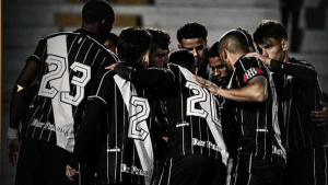 Grupo de jogadores de futebol com camisas pretas e brancas, números grandes nas costas, reunidos em meio a conversas e concentração durante um jogo ou treino em ambiente externo