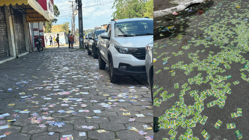 Via pública com veículos estacionados e uma grande quantidade de santinhos de políticos sobre o asfalto em ambiente urbano ao ar livre.