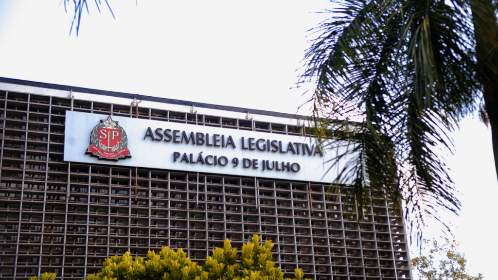 Fachada da Assembleia Legislativa no Palácio 9 de Julho, com a placa “ASSEMBLEIA LEGISLATIVA” e “PALÁCIO 9 DE JULHO” visível ao lado de janelas e da entrada do prédio.