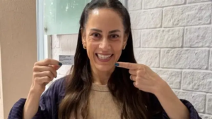 Silvia Abravanel em ambiente interno, usando blusa bege e jaqueta azul, em frente a parede clara de tijolinhos