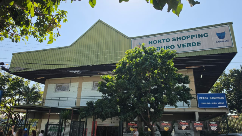 Entrada do Horto Shopping e do Horto Verde, com fachada de prédio verde e grande placa de identificação, árvores e céu azul ao fundo em Campinas.