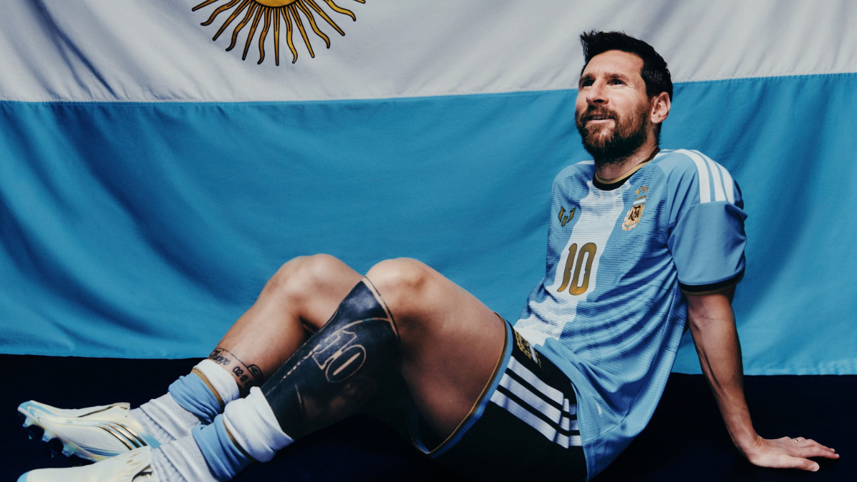 Messi com o uniforme da Argentina e ao fundo, a bandeira de seu país.