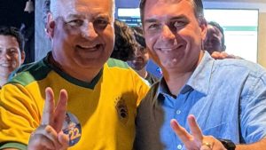 Alfredo Gaspar e Flávio Bolsonaro aparecem juntos em evento político e fazem o gesto de dois com as mãos.