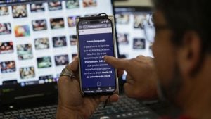 Governo bloqueia cerca de 13,2 mil sites de bets ilegais: homem acessa no celular uma tela de “Acesso bloqueado” enquanto usa computador com imagens de entretenimento ao fundo.