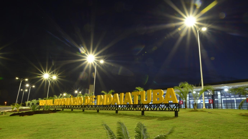 Placa com o nome “INDIATUBA” e gramado em primeiro plano, em uma área externa iluminada por postes de luz sob o céu noturno, com estrutura ao fundo.