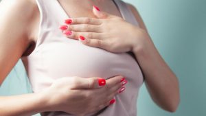 Mamografia em Outubro Rosa: mãos femininas seguram carinhosamente o seio sobre um fundo azul, transmitindo cuidado com a saúde da mulher e prevenção.