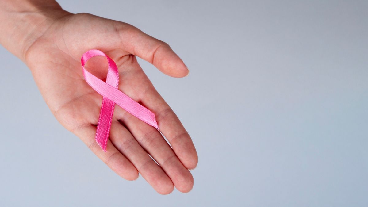 câncer de mama inflamatório: Mão feminina segurando uma fita rosa no peito, simbolizando conscientização sobre câncer de mama; imagem em fundo claro, sem nódulos visíveis, com foco educativo em sinais e alerta