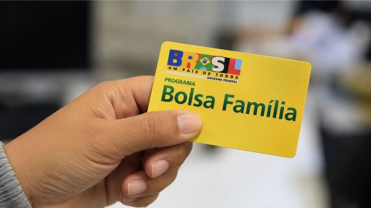 Mão segura cartão amarelo do Bolsa Família em ambiente interno.