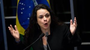 Janaina Paschoal fala com microfone à sua frente. De fundo, uma bandeira do Brasil