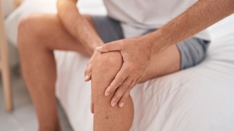 Trombose: homem com a mão massageando a perna e o joelho, em foto de saúde que ilustra sinais e sintomas de alerta, com foco em dor e desconforto.