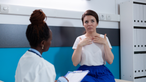 Médica em consulta se preparando para exame de uma paciente em ambiente clínico, com postura de avaliação das mãos e caderno na sala.