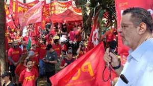 Rui Costa Pimenta discursa em ato do Partido da Causa Operária (PCO), diante de manifestantes com bandeiras vermelhas.