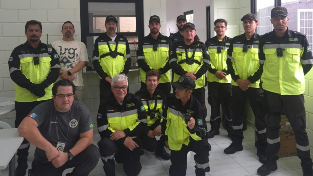 Equipe de trabalhadores uniformizados com coletes de alta visibilidade e roupas de segurança, em ambiente interno, posando para foto em grupo.