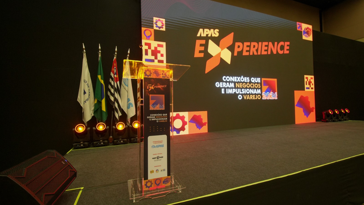 Eexperience APAS 2026 em palco, com telão ao fundo exibindo o tema “Conexões que geram negócios e impulsionam o varejo 2026”, além de bandeiras e iluminação cênica durante o evento.