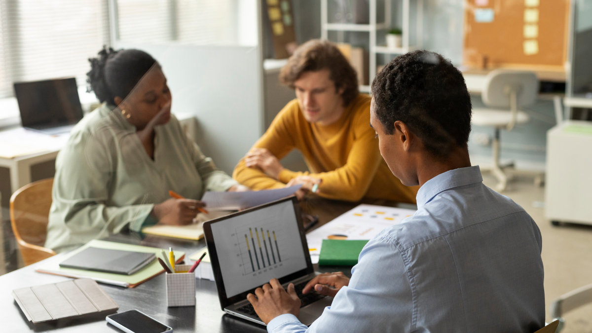 Equipe reunida em escritório moderno, analisando relatórios em tablets e notebooks, com gráficos em telas durante uma reunião de trabalho colaborativa.