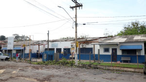 Vista externa CS Paranapanema simples com fachada pintada de azul e branco, cercas e portões, placas de identificação e postes de energia ao longo da rua, sob céu claro.