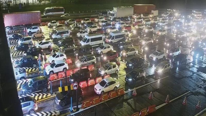 Vista ampla de um grande congestionamento na rodovia da Imigrantes movimentada, com muitos carros e caminhões parados em meio à sinalização e faixas de trânsito durante a noite.