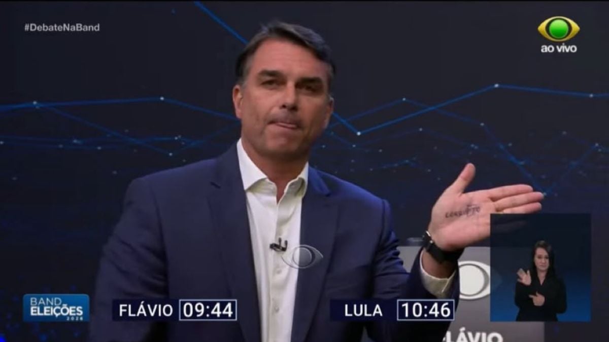 O que está escrito na mão de Flávio Bolsonaro durante debate com Lula na Band?
