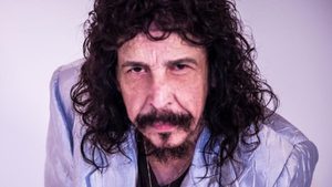 Benito di Paula em foto retrato, com cabelo e barba encaracolados, olhando para a câmera em um fundo claro, expressão séria.
