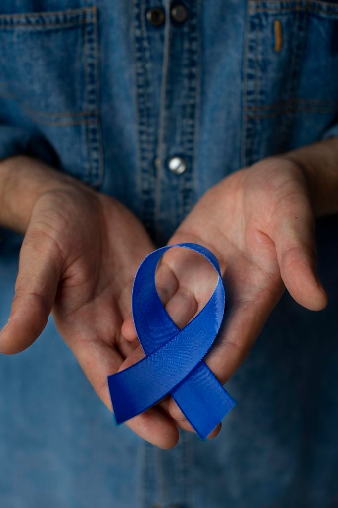 Homem segura um laço azul na mão, símbolo de conscientização sobre saúde e apoio à causa do câncer de próstata.