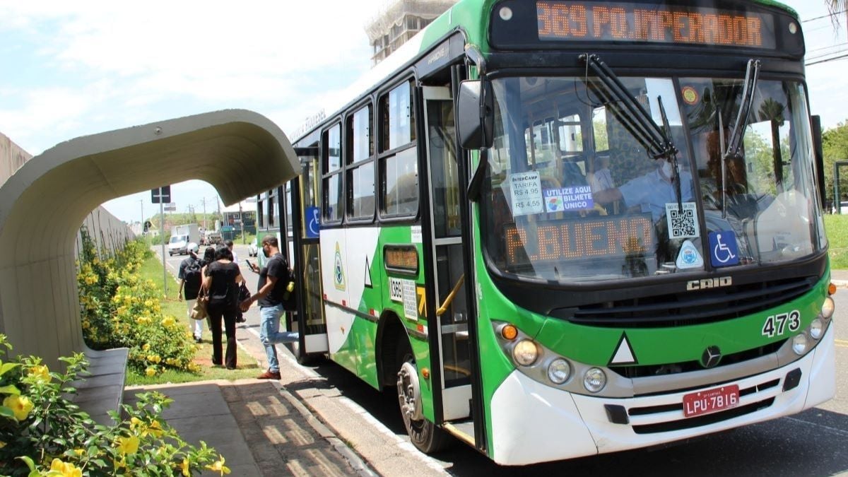 Ônibus urbano verde e branco com acessibilidade, placa e número 473, parado em ponto de embarque ao lado de pessoas em ambiente externo com flores e calçada.