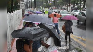 Legenda: Pedestres utilizam guarda-chuvas durante período de chuva em Santos, na Baixada Santista.Crédito: Carlos Nogueira/Prefeitura de Santos